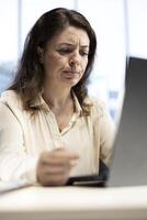 Overburdened entrepreneur in discomfort feeling tired and worried, working hard to meet deadline and protect her business. Young CEO being stressed and uncomfortable, overload. photo