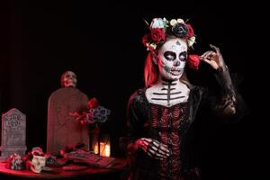 Woman with flower at Day of the Dead event with spooky decor to remember the deceased, celebrating their memory. Lady holding red rose for traditional holiday of remembrance for those who have passed photo