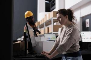 Stockroom manager checking customer order on computer, discussing shipping details with african american worker in storehouse. Diverse team working at merchandise quality control in warehouse photo