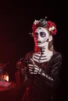 Woman playing games with gamepad, during Dia de los Muertes indigenous rites of honoring the dead. Lady enjoying videogames with controller during Day of the Dead, Mexico event in honor of deceased photo
