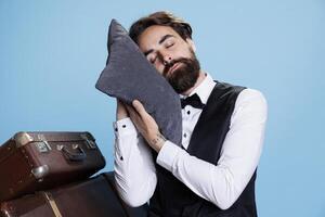 Hotel worker falls asleep on a pillow with pillow on camera, expressing burnout and feeling sleepy at professional classy job. Doorman taking quick nap after being overworked, exhausted doorman. photo