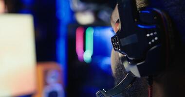 Man playing SF videogame on computer, having fun in neon lit apartment, close up. Gamer competing in online multiplayer game, using headphones to talk with teammates, camera B photo