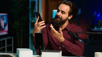 Entertainer presents smartphone from sponsoring brand, closely analyzing features. Content creator reviewing phone for tech enthusiasts watching his internet channel, inspecting materials, camera A photo