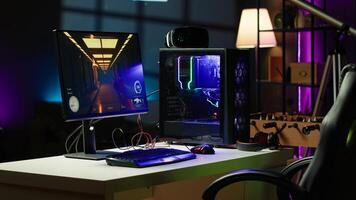 Empty apartment living room with neon lights and gaming computer with first person shooter game left open on monitor. Singleplayer videogame on desktop pc display on desk late at night photo