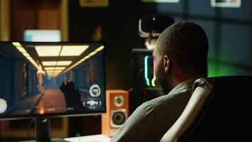 Man in neon lit apartment playing immersive games on gaming PC at computer desk, handheld camera shot. Gamer competing against enemies in internet multiplayer shooter, camera A photo