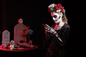 Girl texting friends on smartphone at Dia de los Muertes indigenous rites of honoring the dead. Woman checking social media on phone, participating at Day of the Dead in honor of the deceased photo
