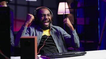 Merry man feeling happy while playing videogames on gaming PC, celebrating victory. Player excited after winning computer game, displaying happiness emotions, shaking fist, camera A photo