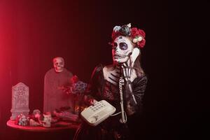 Woman using landline phone to answer call during Day of the Dead Mexican event honoring dead loved ones. Person talking on office cord telephone during ancient Aztec custom of celebrating ancestors photo