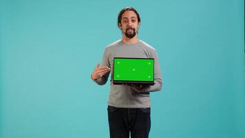 Man presenting green screen mobile laptop, isolated over studio background. Arab person holding copy space chroma key notebook device used for advertising brands, camera A photo