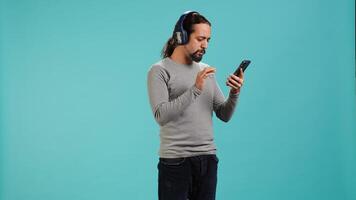 Relaxed man having fun listening to music from mobile phone, studio backdrop. Carefree person hearing tunes playing from smartphone device, isolated over studio background. camera A photo