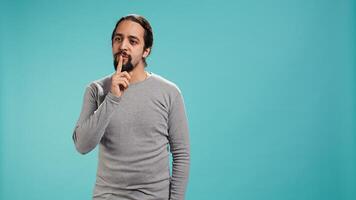 Annoyed man doing shushing hand gesturing, irritated by noise, having negative mood. Person placing finger on lips, doing quiet sign gesture, isolated over studio background, camera B photo