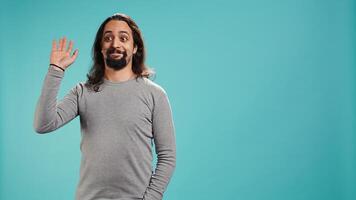 Smiling man greeting friends, happy to see them, isolated over blue studio background. Friendly person waving hand, saluting mates, being friendly, studio backdrop, camera B photo