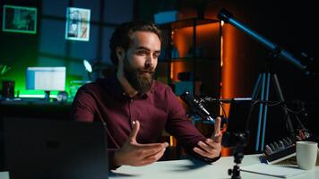 Media star talking in front on smartphone attached to tripod stabilizer in studio, discussing with viewers. Man using mobile phone to record in living room for social media, camera B photo