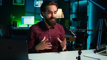 Influencer talks in front on smartphone attached to tripod and high quality mic in studio, discussing with viewers. Man using mobile phone and professional gear to record social media , camera B photo