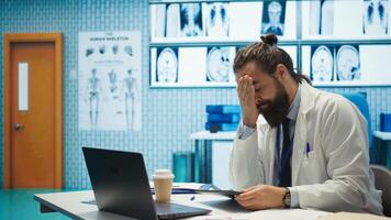 Tired worried doctor working after hours to find the diagnostic for a patient, feeling very stressed and trying to examine x ray results in medical cabinet. Frustrated overworked medic. Camera B. photo
