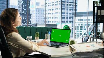 Business director working in her own office with green screen, looking at device display and developing a new project idea. Female entrepreneur empowered by corporate culture. Camera A. photo