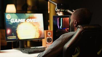Gamer losing intense singleplayer spaceship arcade racing videogame, seeing game over screen on capable gaming computer system at home. Man upset after being defeated on difficult game level, camera A photo