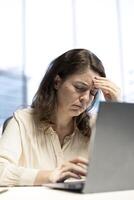 Exhausted overwhelmed businesswoman with a headache trying to meet project deadline, working hard to save the reputation of her corporation. Stressed nervous leader in crisis, overload. photo