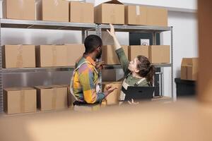 Diverse warehouse team checking cardboard boxes, working at customers orders before start shipping packages. Employees doing products quality control, discussing inventory report in storehouse photo
