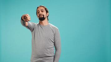 Upset man showing thumbs down sign gesturing, being disapproving. Disappointed Arab person against gaming, doing rejection hand gesture, isolated over studio background, camera B photo