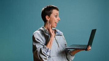 Trendy cool woman waving on a videocall connection in studio, using her laptop to attend an online remote meeting. Friendly person chatting on conference call. Camera A. photo