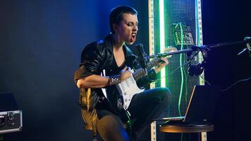 Pleased punk rock artist rehearsing for her live performance, focusing on vocal training and warm up. Edgy iconic woman enjoying singing practice with alternative music. Camera A. photo