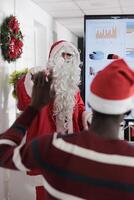 Public speaker dressed as Santa Claus for Christmas meeting event in festive adorn workspace during winter holiday season. Participant raising hand to ask question about best ways to improve company photo
