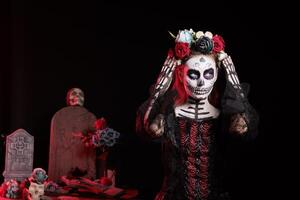Woman participates in Day of the Dead Mexican event honoring dead loved ones, building altar for them. Lady doing ancient Aztec custom of celebrating ancestors, putting on flower crown photo