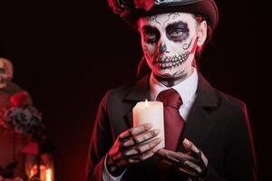 Woman lighting candle during Day of the Dead Mexican event honoring dead loved ones. Portrait of person with candlestick on fire during ancient Aztec custom of celebrating ancestors photo