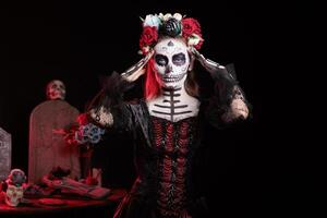 Woman at Day of the Dead event to remember the deceased and celebrating their memory, graveyard background. Lady wearing skull makeup for mexican holiday of remembrance for those who have passed photo