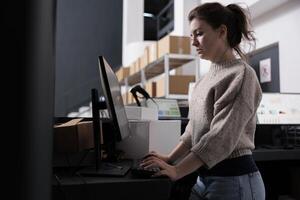 Warehouse manager standing at counter desk, analyzing merchandise logistics on computer. Stockroom worker checking customers online orders preparing packages for shipping in storehouse photo