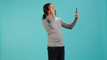 Smiling man having friendly conversation with friends during teleconference meeting using smartphone, studio background. Person having fun catching up with mates during online videocall, camera A photo