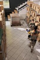 Diverse team discussing about invoice code on tablet trying to find customer parcel in storage room. Warehouse employee wearing protective overall while preparing orders for delivery. Aerial view photo