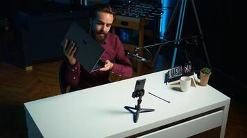 Tech expert assessing laptop performance, talking about components used inside, filming with smartphone. Entertainer reviewing notebook on technology internet channel, recording with phone, camera B photo