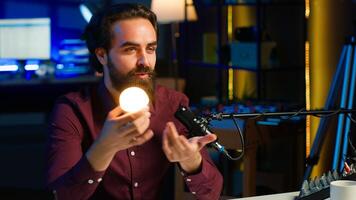 Smart light bulb used by tech specialist in studio to teach audience how to fix it, handheld camera shot. Focus on IoT home automation product held by media star, camera A photo