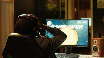 Heartbroken gamer dejected after losing in online multiplayer videogame, being defeated by rivals. Man putting hands on head in frustration after seeing game over screen on gaming pc monitor, camera A photo