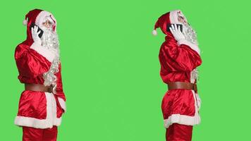 Saint nick answering phone call on camera, talking to someone on smartphone mobile line for remote conversation. Young man portraying santa claus having chat in greenscreen studio. photo