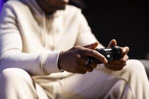 Close up shot of gamepad held by man playing entertaining videogame in rgb lit apartment. Focus on joystick used by person in blurry background to enjoy gaming on console system photo