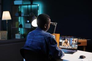 Young black woman engrossed in call with multiracial people, having online meeting. African american person with digital laptop is seated at desk on conference call with fellow classmates. photo