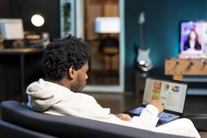 African american self employed man working in personal office, checking statistical data financial graphs on laptop screen. Remote worker in apartment comparing business graphic economic figures photo