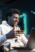 BIPOC man having fun, adding payment method on website while in apartment living room. Joyous person delighted to do online shopping, carefully typing credit card information photo