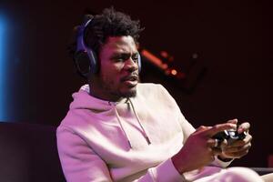 Focused BIPOC man plays intense online videogame, spamming attack buttons on controller. Gamer participating in internet esports competition, sitting on couch and playing on gaming console photo
