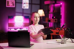 Happy child showing audience mechanical keyboard received from sponsoring brand to promote it. Young internet star advertising wireless Bluetooth computer peripheral from partnering company photo
