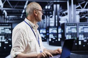 Proficient supervisor using laptop, setting up high bandwidth dedicated multiplayer gaming servers in supercomputer hub to accommodate more traffic from worldwide locations and avoid low ping photo