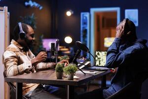 Young interviewer adjusting the sound mixer while talking with guest, recording a talk show. Two african american men using podcast equipment, discussing different topics for their online audience. photo