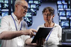 Senior trained wiremen running analysis on blade servers helping businesses manage databases, host websites and store files. Competent electricians auditing high tech data center electronics photo