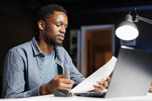 Management student examining business statistics on files, learning to deal with executive responsibilities or finances. African american guy studying contract terms at home desk. photo