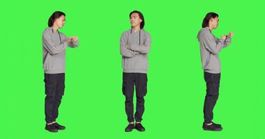 Impatient adult waiting for something in studio, looking around and checking hour on wristwatch over greenscreen backdrop. Asian person being unhappy and irritated, looks at watch. photo