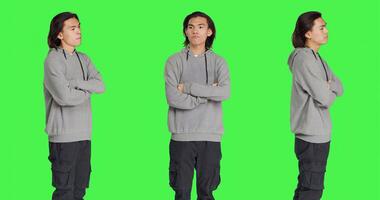 Impatient person waiting for something in studio, looking around and checking time on wristwatch over greenscreen background. Asian man being grumpy and snappy, looks at watch. photo