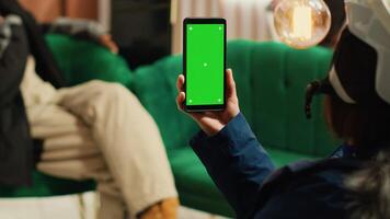 Person uses smartphone with greenscreen and enjoying conversation with boyfriend, showing blank chromakey display on phone. Diverse couple at alpine skiing resort during wintertime. photo